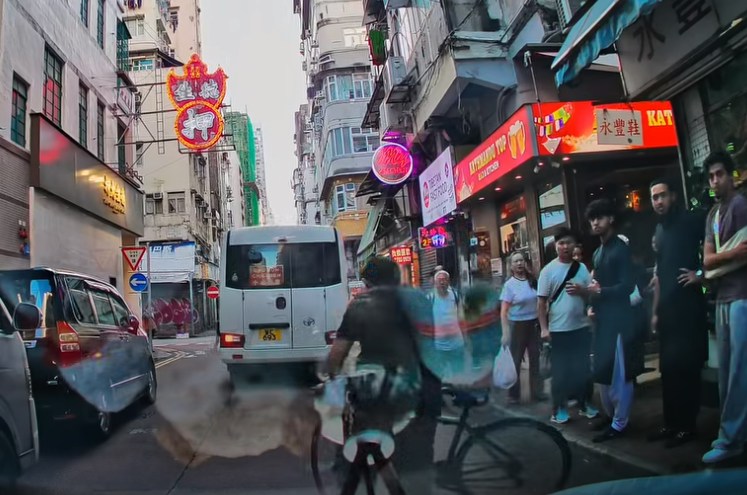 CAM车途经油麻地西贡街时,一名非华裔男子从右方推着单车走到马路中间,其后骑上单车。惟该男子驶前不久,一个身穿浅蓝衣的人突然手持长棍从后方冲出,朝单车男追打。(fb/车cam L(香港群组))